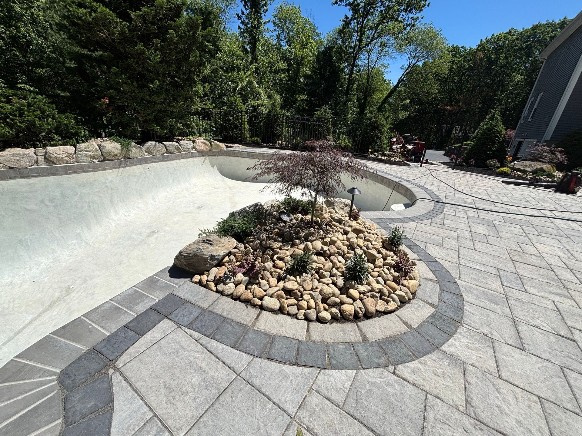 Stone patio with a circular raised planter and dry creek bed in a sunny landscaped yard