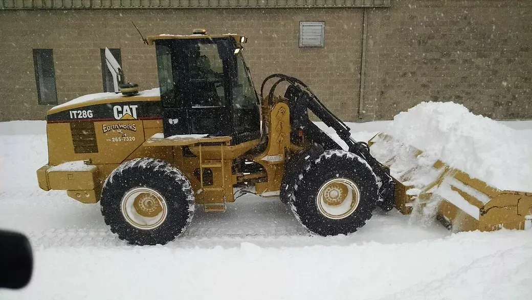 A yellow Caterpillar wheel loader pushing a large pile of snow in a snowy, outdoor setting.
