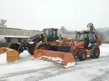 Two orange and black backhoe loaders parked on a snow-covered lot with snowplow attachments.
