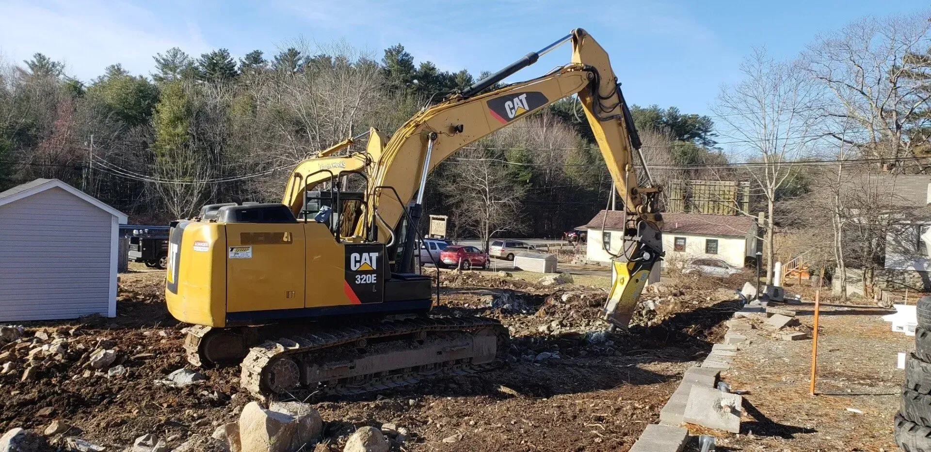 A yellow Caterpillar excavator digging in a dirt-filled construction site with a small building in the background.