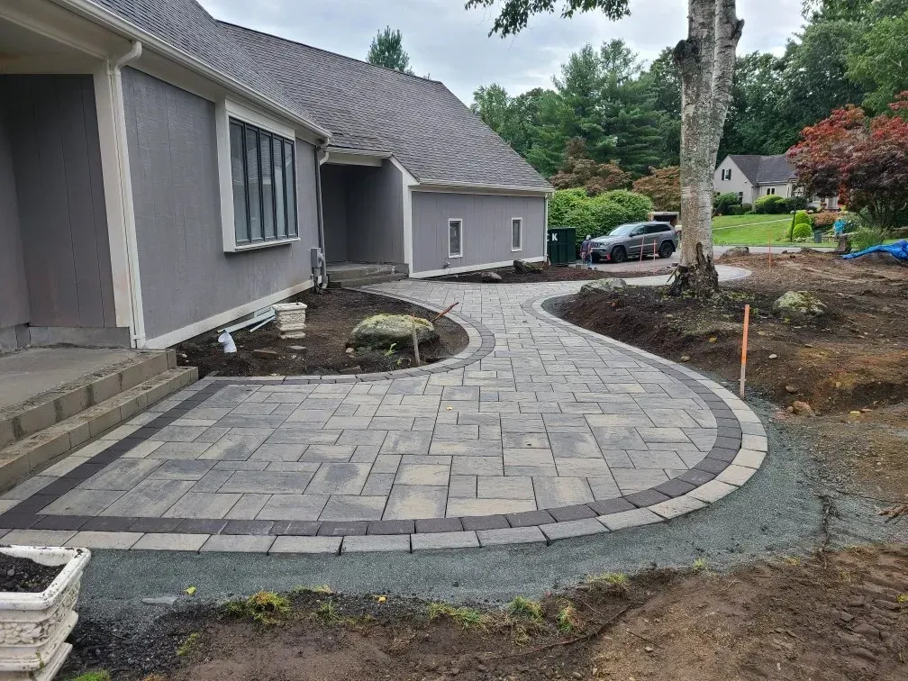 A gray house with a newly installed curved stone paver walkway and patio leading to the front steps.