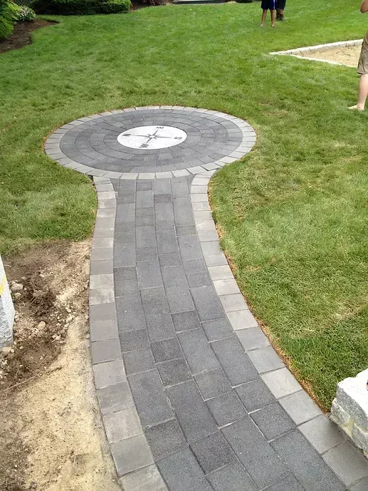 A stone walkway leads to a circular patio feature with an inlaid compass rose, set in a grassy backyard.