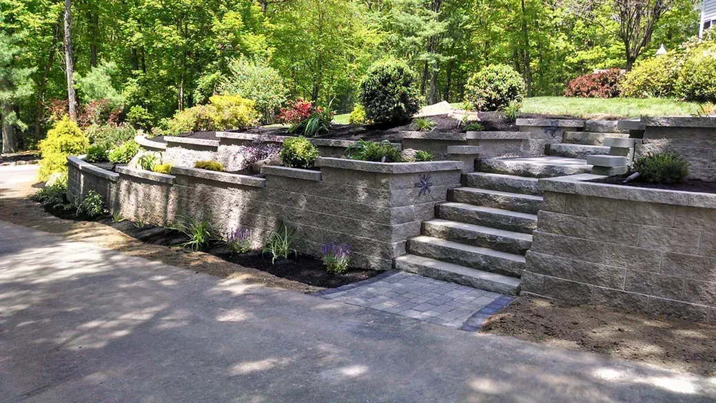 A tiered stone retaining wall with integrated steps leading up into a landscaped, tree-filled garden.