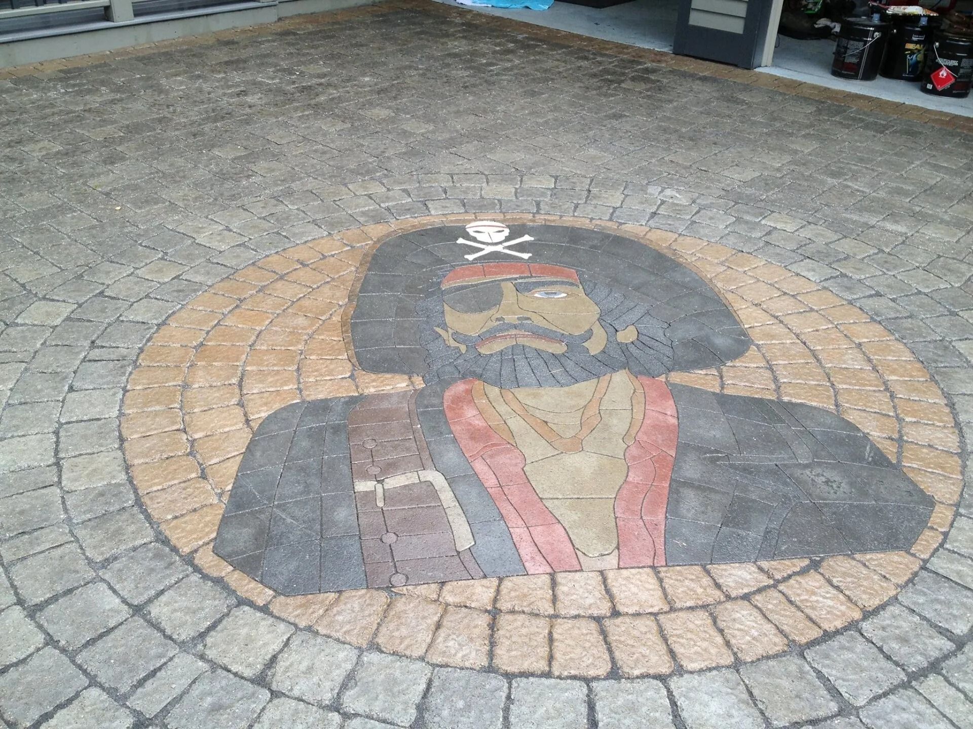 A mosaic of a pirate wearing an eyepatch and hat, designed with colored paving stones on a patio.