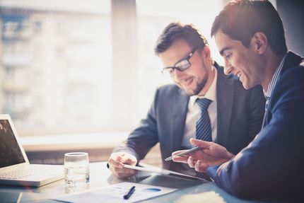 Two business people reviewing documents at a laptop in a bright office