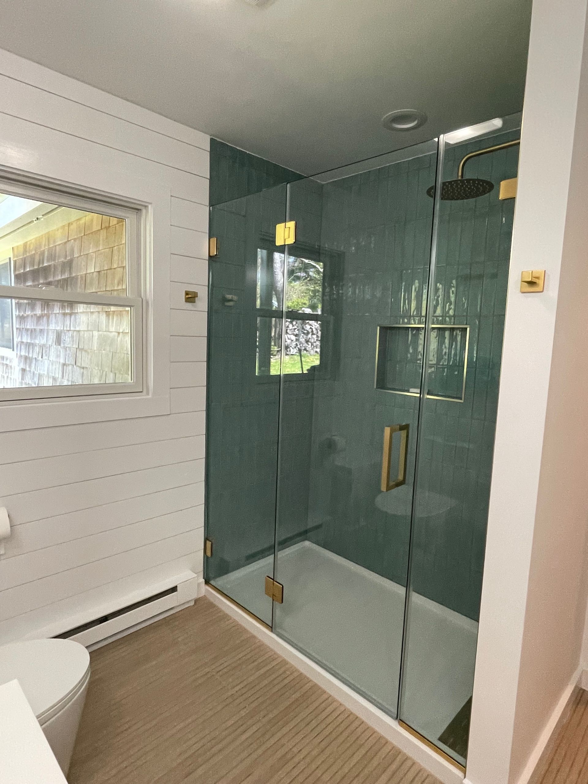 Glass shower enclosure in a bright bathroom with white walls and beige flooring