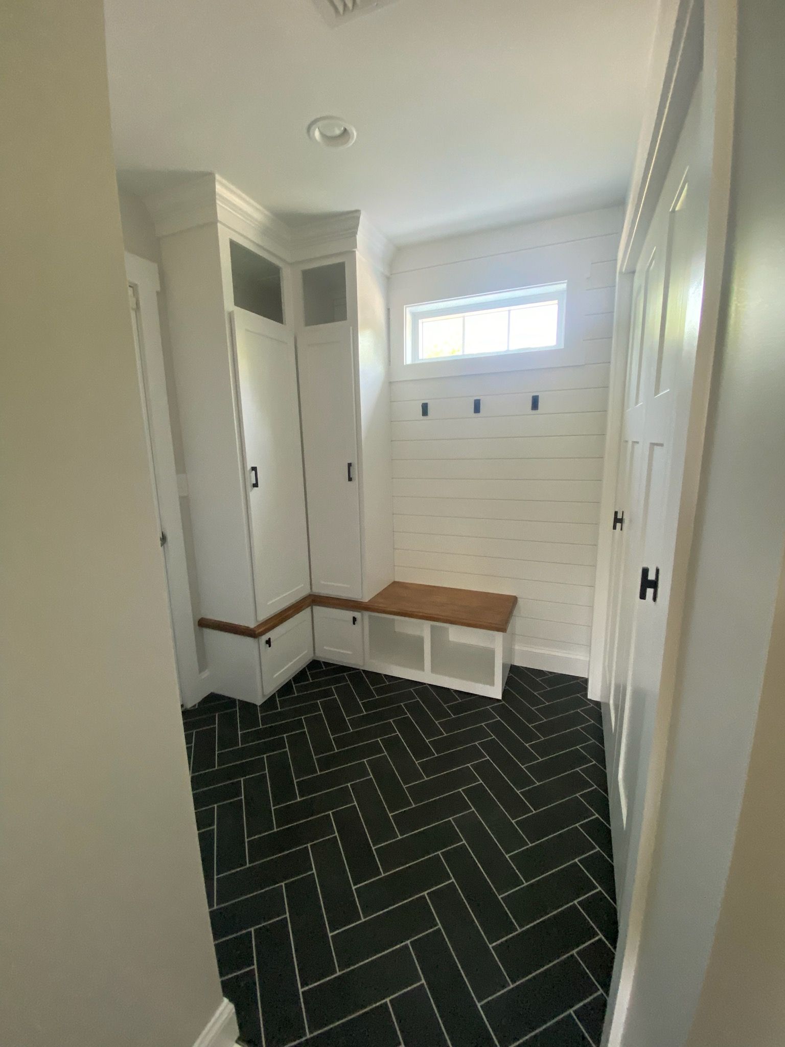 Small entryway with white walls, black patterned carpet, built-in bench, and a high window.