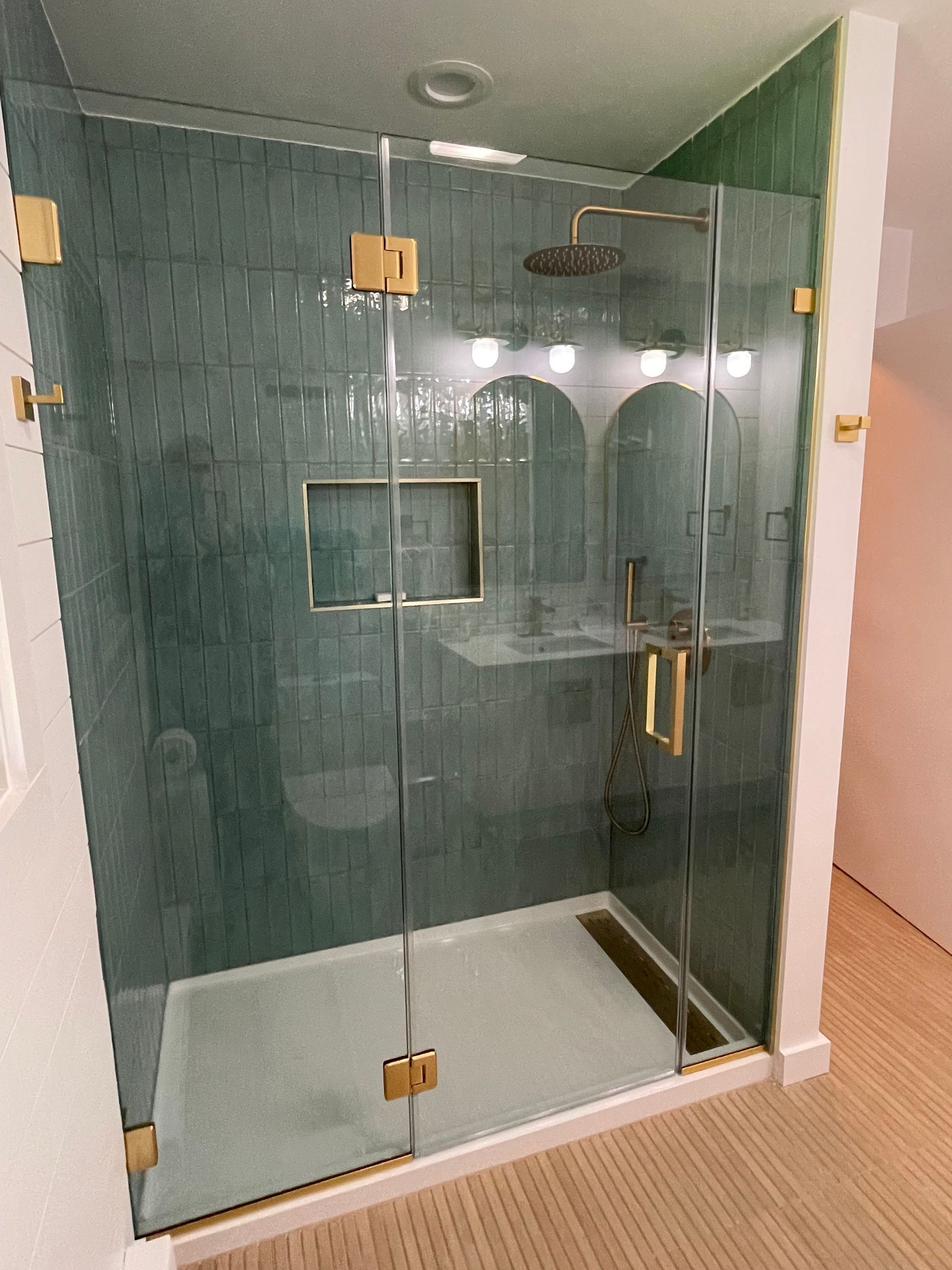 Modern glass shower enclosure with green tile walls and white tub base