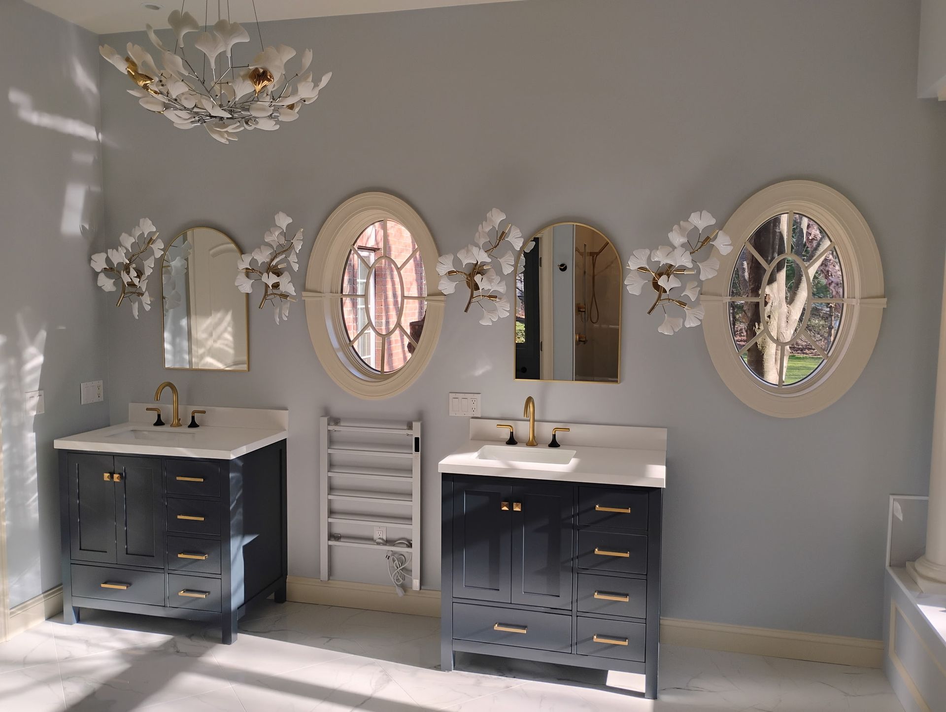 Modern bathroom with twin navy vanities, oval mirrors, and orchid wall decor on gray walls