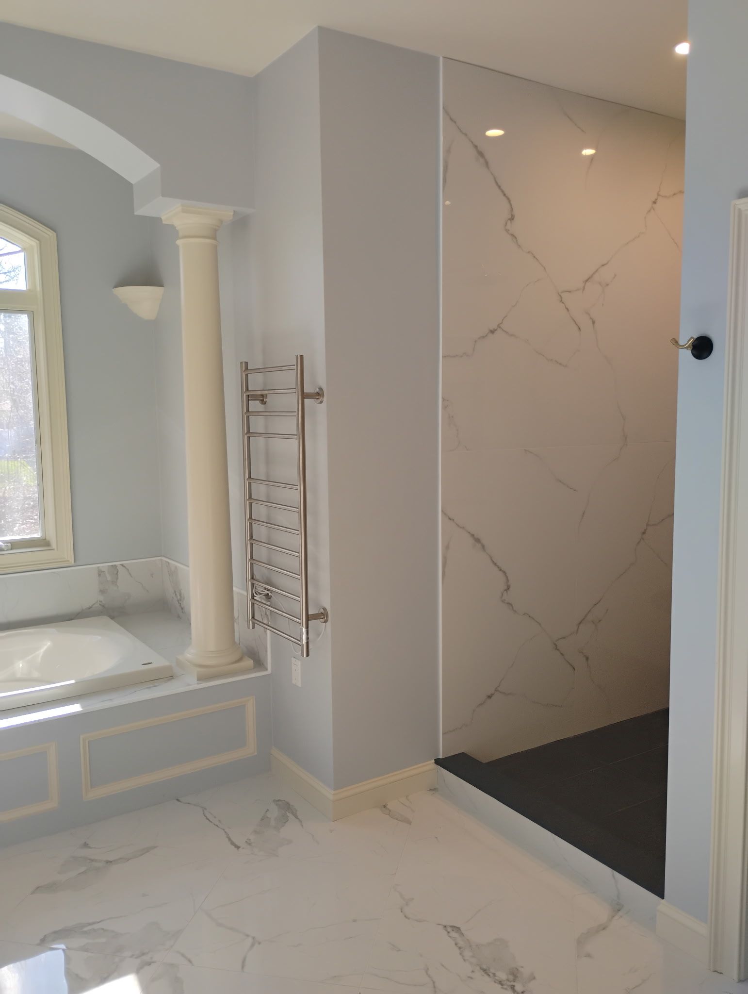 Bright bathroom with marble shower, white column, and an open doorway to a lit walk-in shower.