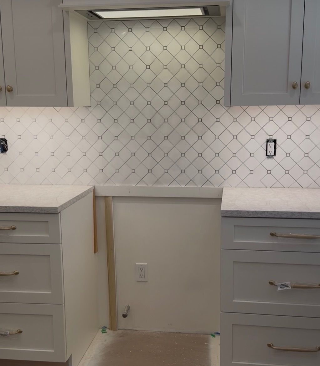 Kitchen backsplash installation with white tile and gray cabinets around an unfinished center opening