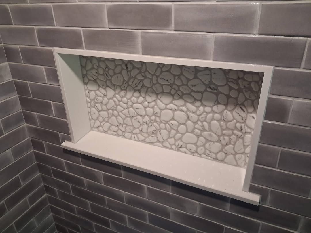 Small recessed wall shelf with white trim, set in a dark gray tiled wall.