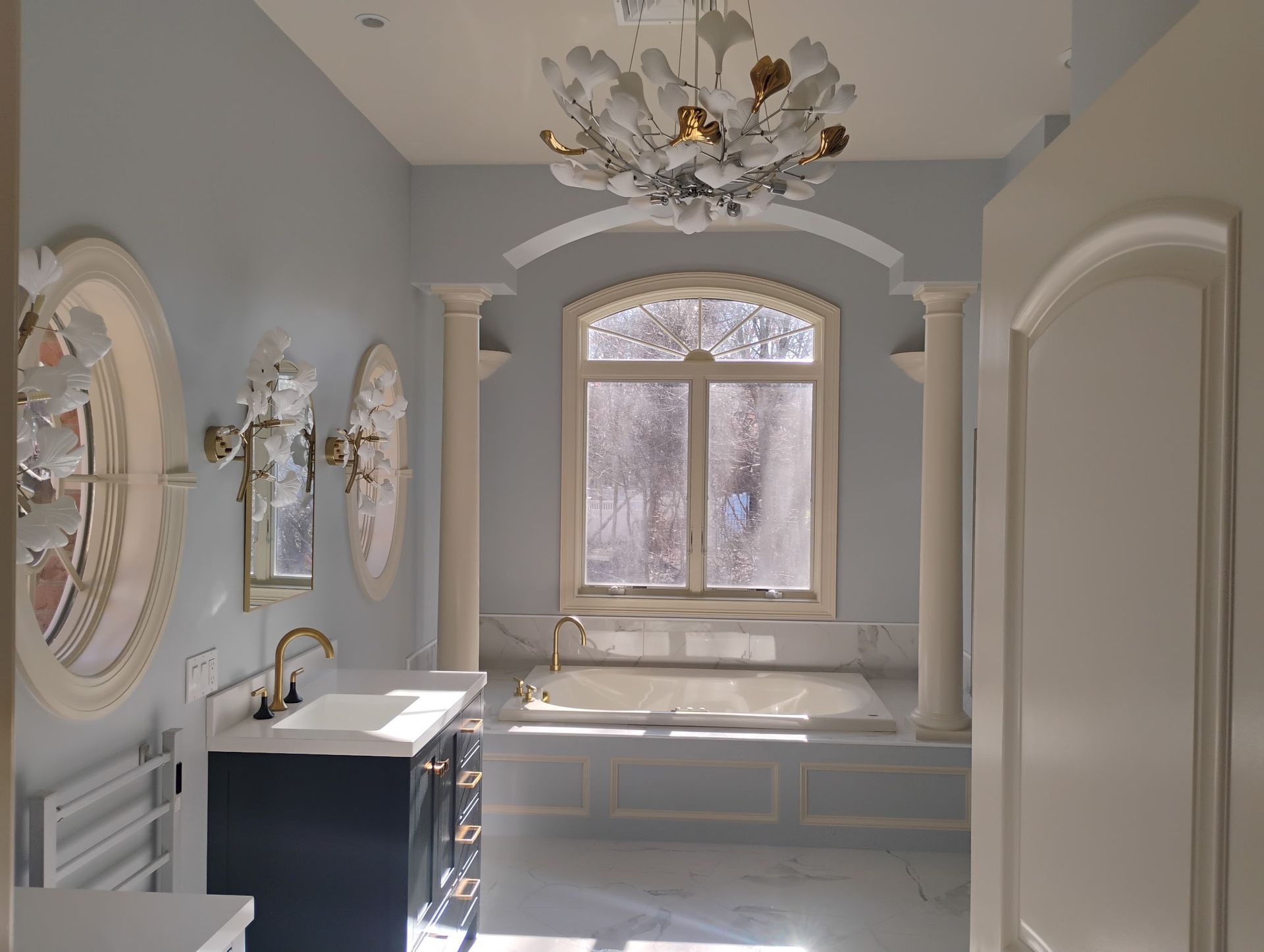 Elegant gray bathroom with a freestanding tub, large window, and chandelier chandelier-style ceiling light