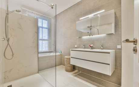 Learn More About Tile Modern beige bathroom with glass shower, white vanity, mirror, and window blinds
