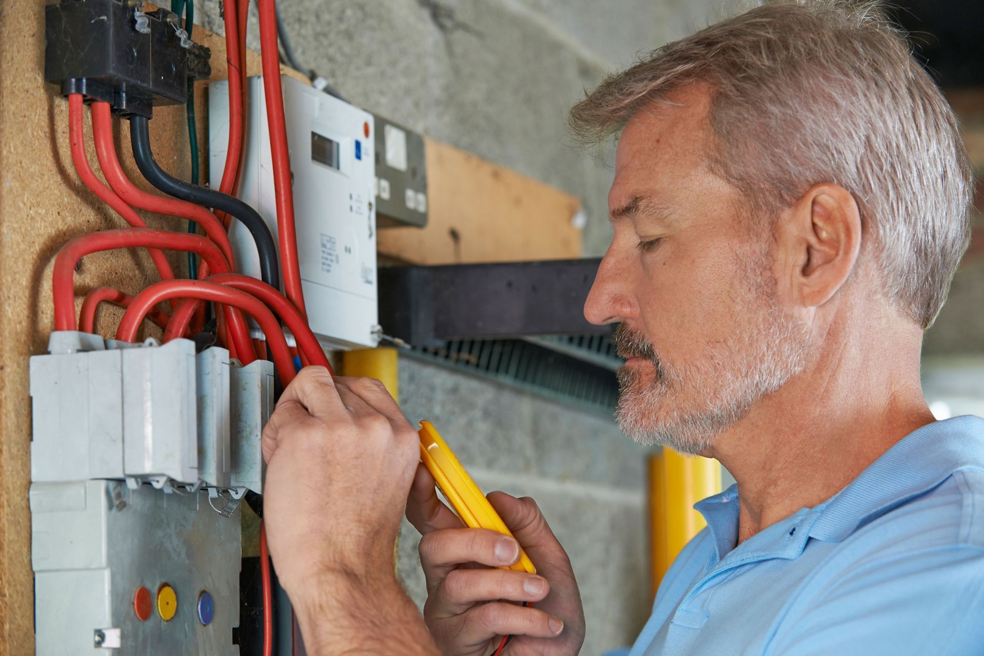 A man is working on an electrical box with a voltmeter.