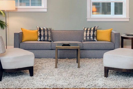 A living room with a couch , chairs , ottomans and a rug.