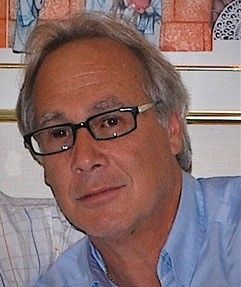 A man wearing glasses and a blue shirt is sitting on a couch.