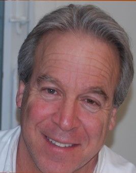 A man with gray hair is smiling and wearing a white shirt.