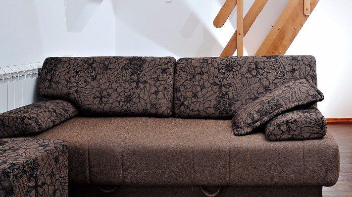 A brown couch in a living room with stairs in the background