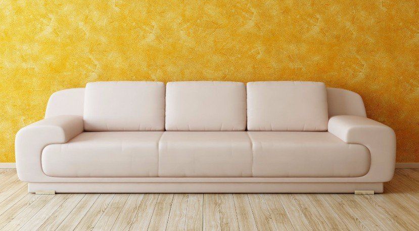 A white couch is sitting in front of a yellow wall in a living room.