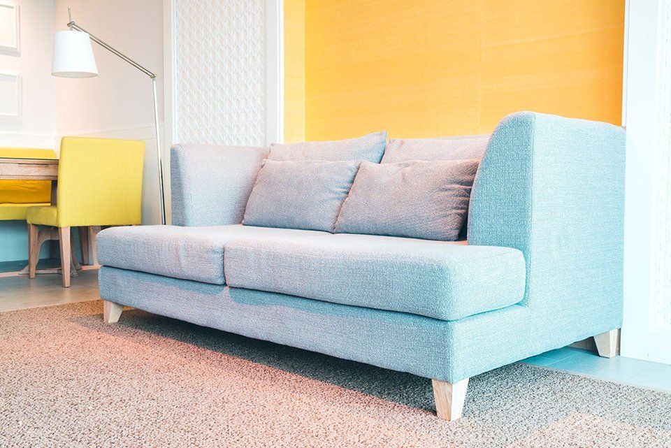 A blue couch is sitting in a living room next to a yellow wall.