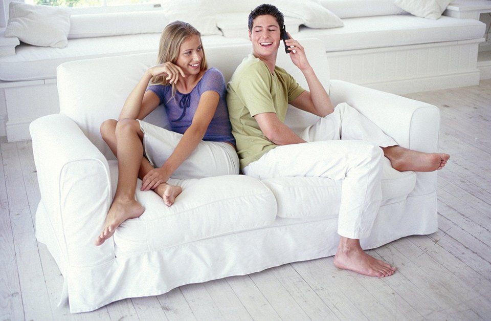 A man and a woman are sitting back to back on a white couch