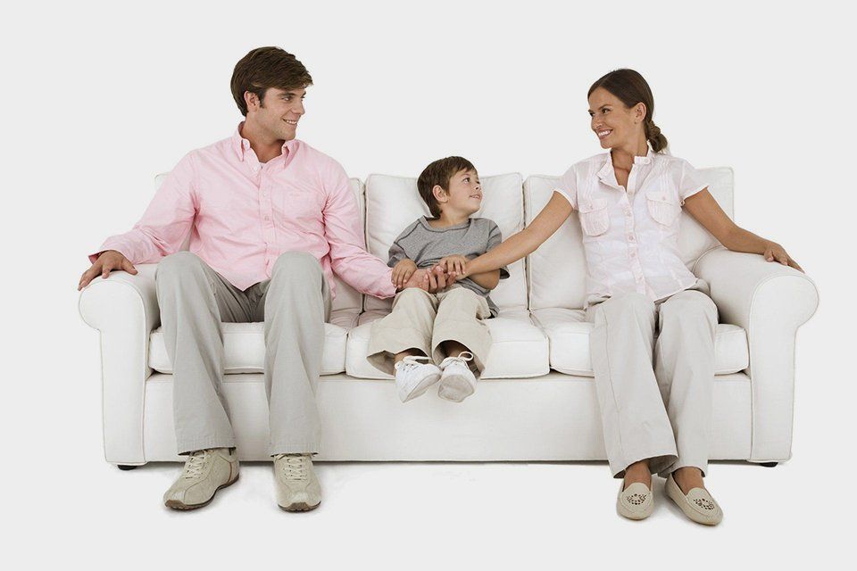 A family is sitting on a white couch holding hands