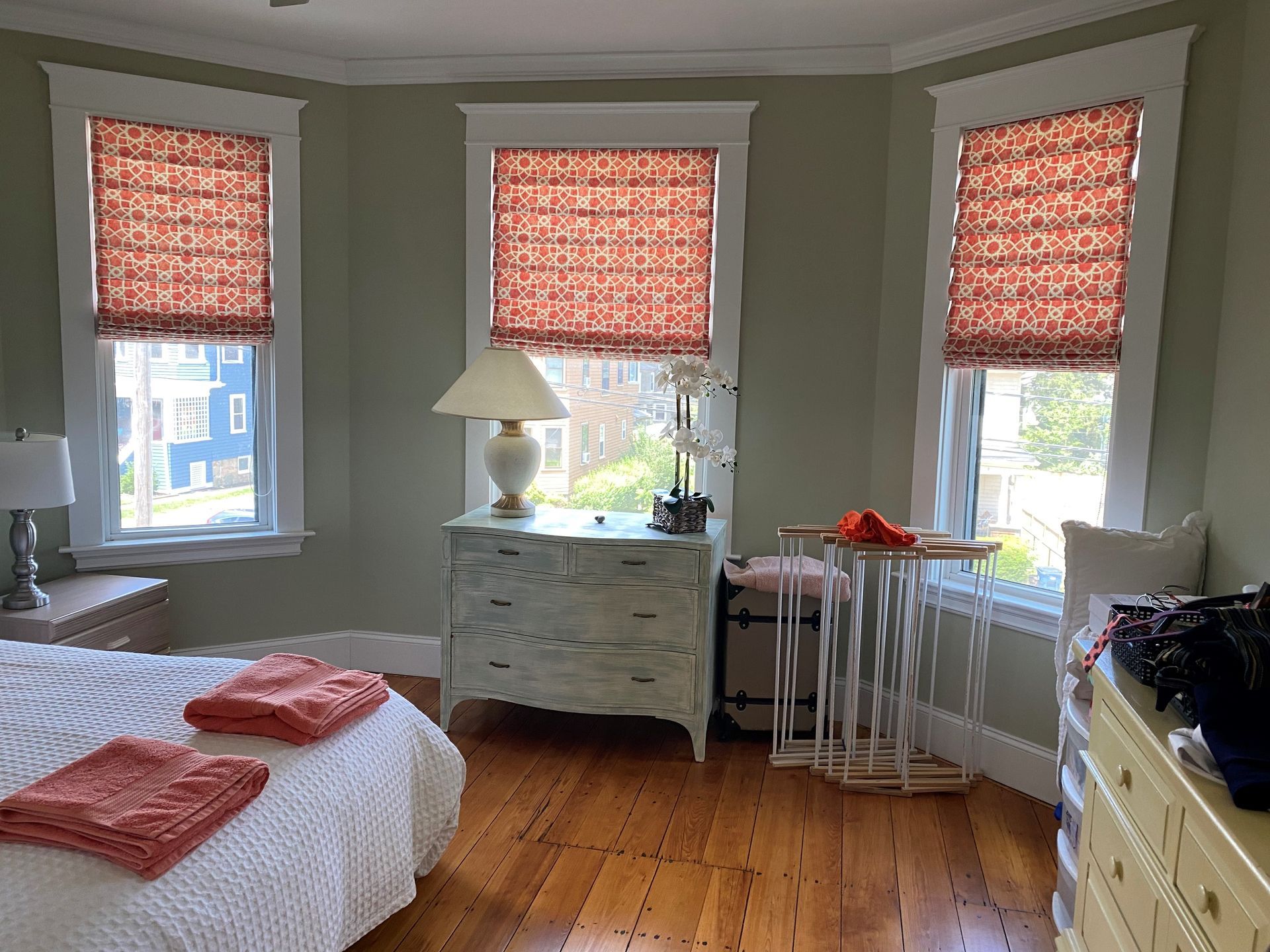 A bedroom with a bed , dresser , lamp and two windows.