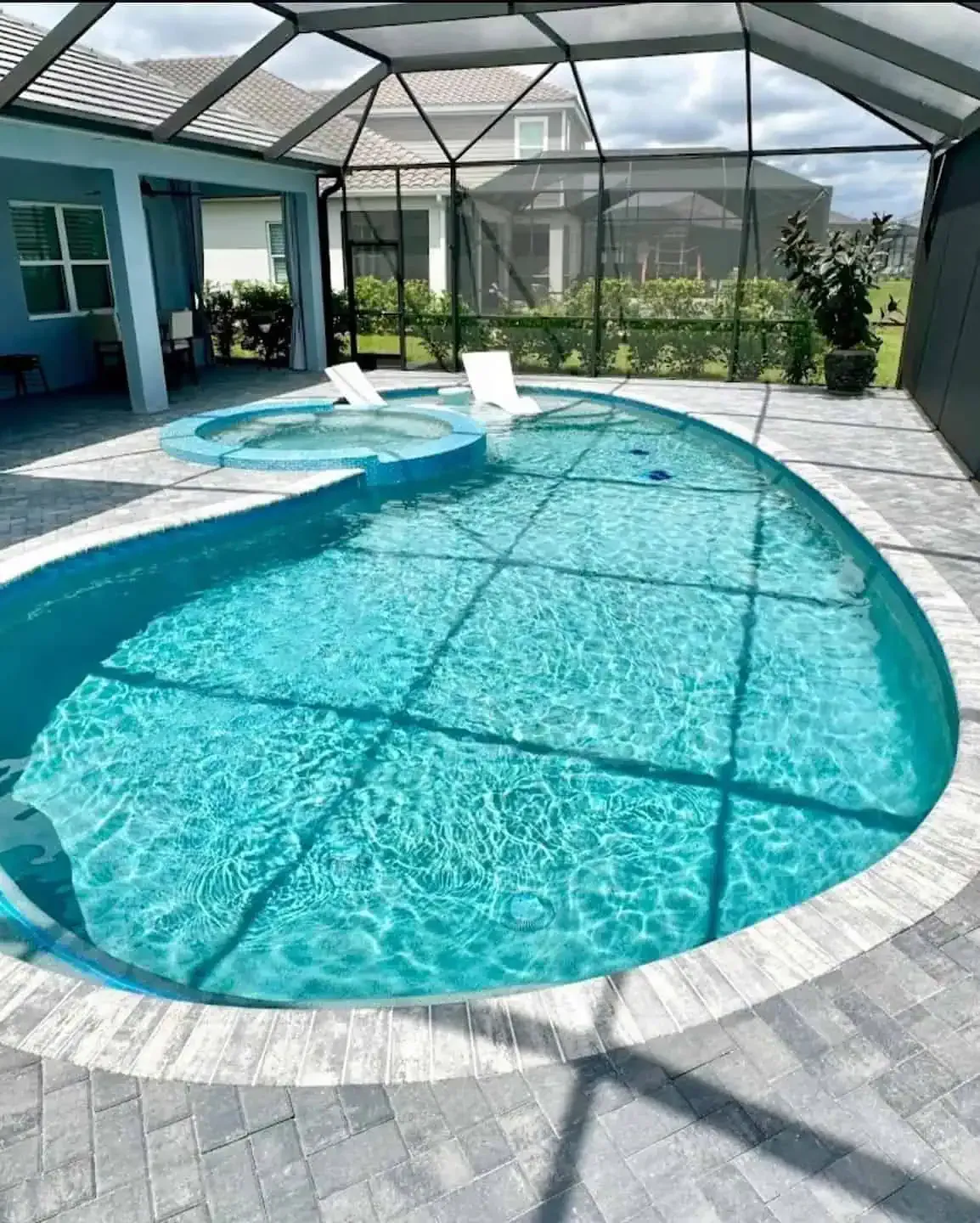 Indoor screened pool with turquoise water, white lounge chairs, and a gray tile deck