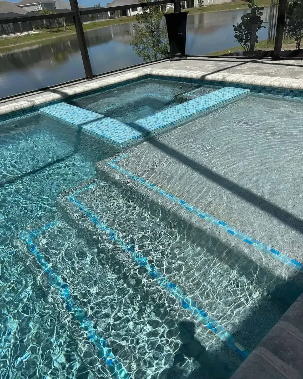 Blue-tiled swimming pool with shallow steps and sparkling water beside a canal