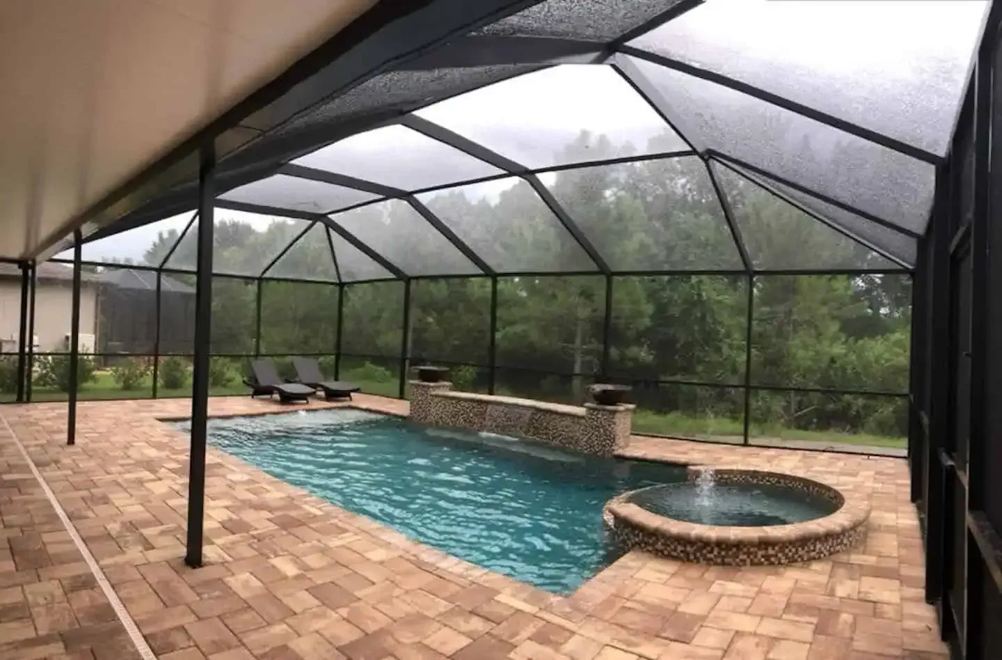 Screened-in backyard pool with brick patio and attached hot tub under a covered lanai