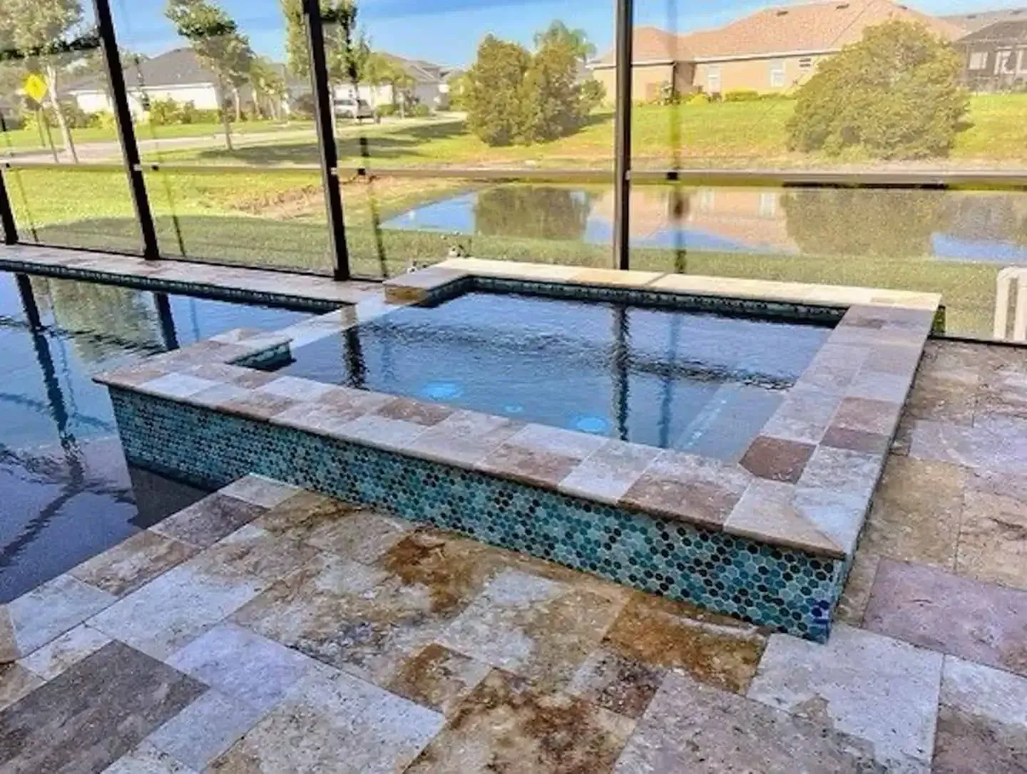 Modern outdoor spa with tiled seating and water, overlooking a landscaped pond and grassy park.