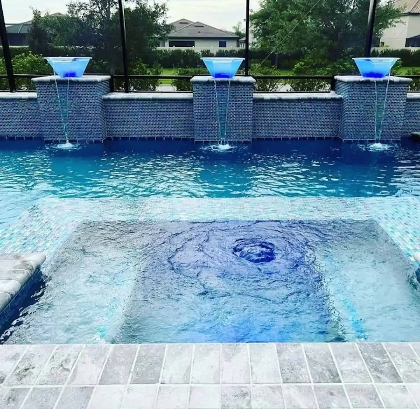 Backyard pool with a shallow spa, blue waterfall fountains, and a tiled deck