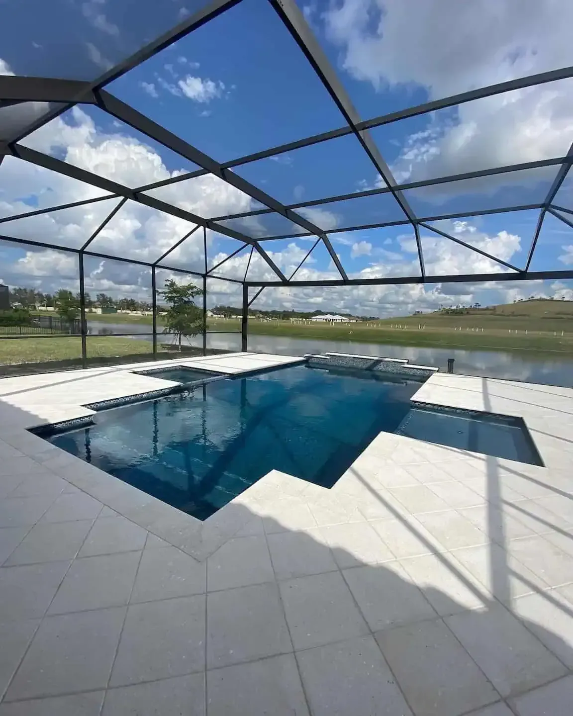 Screened backyard pool with blue water, white tile deck, and open sky view over grassy fields
