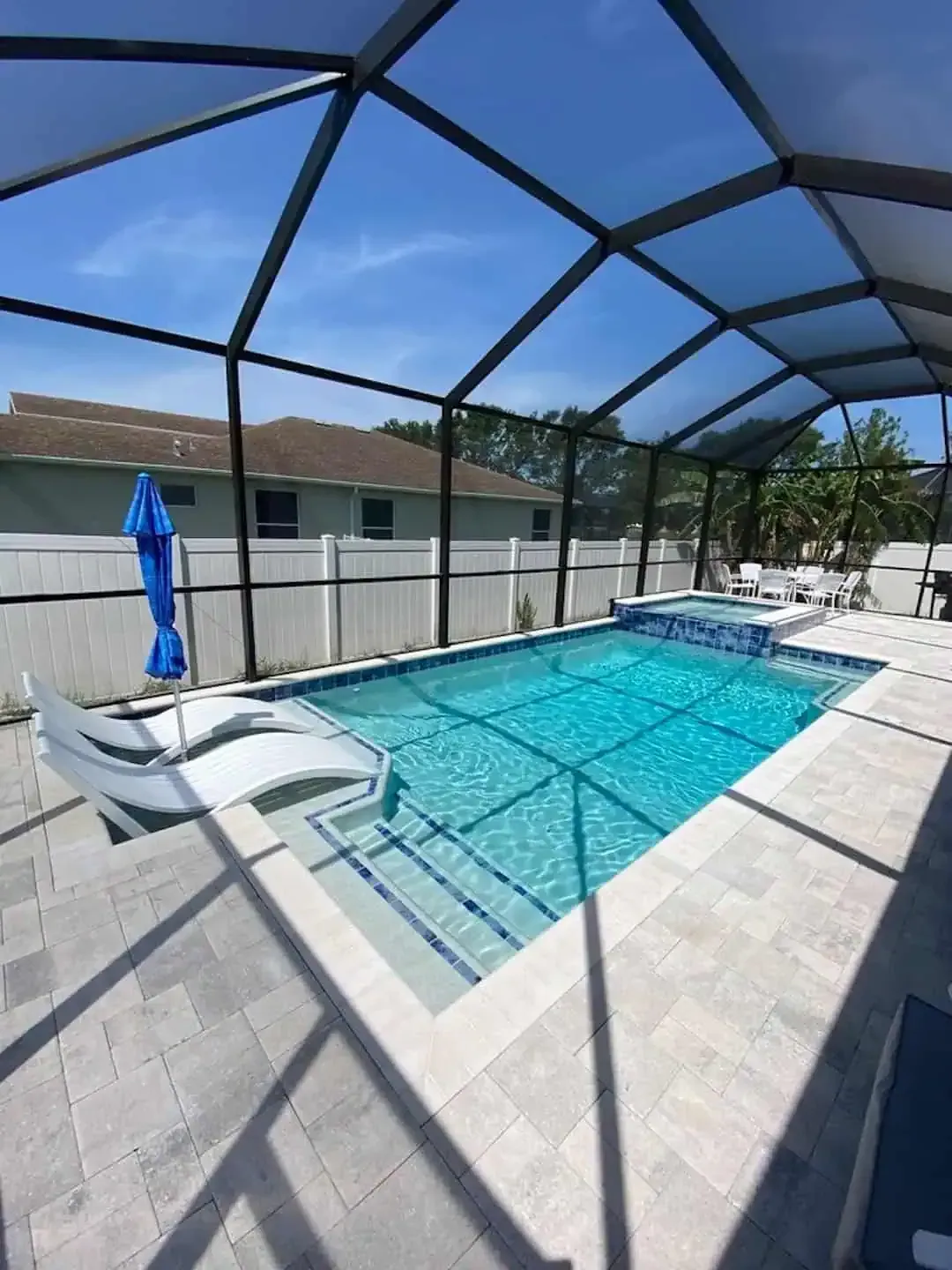 Covered backyard pool with blue water, white lounge chairs, and a screened enclosure under a sunny sky