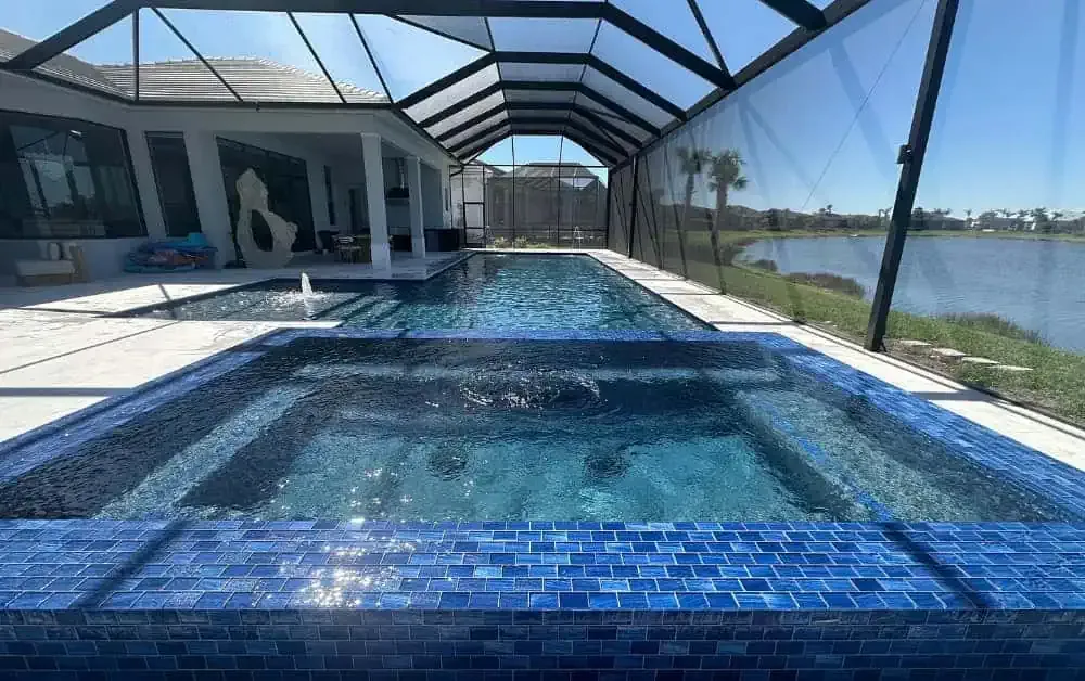 Covered backyard pool with blue tile, glass enclosure, and water view on the right.