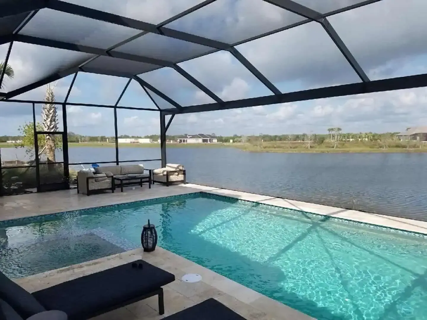 Covered patio with a turquoise pool overlooking a calm waterfront.