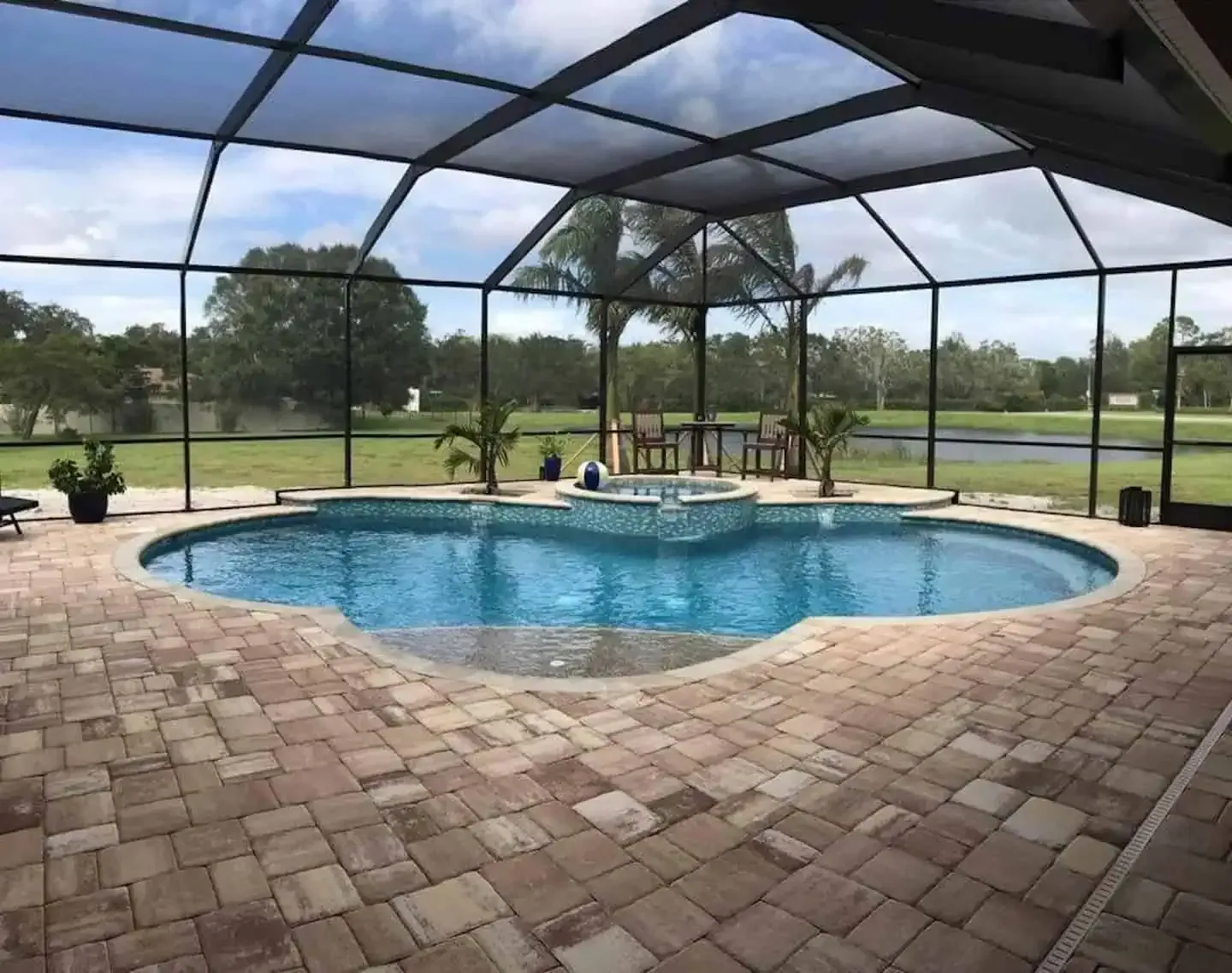 Screened-in backyard pool with brick patio and patio furniture under a blue sky