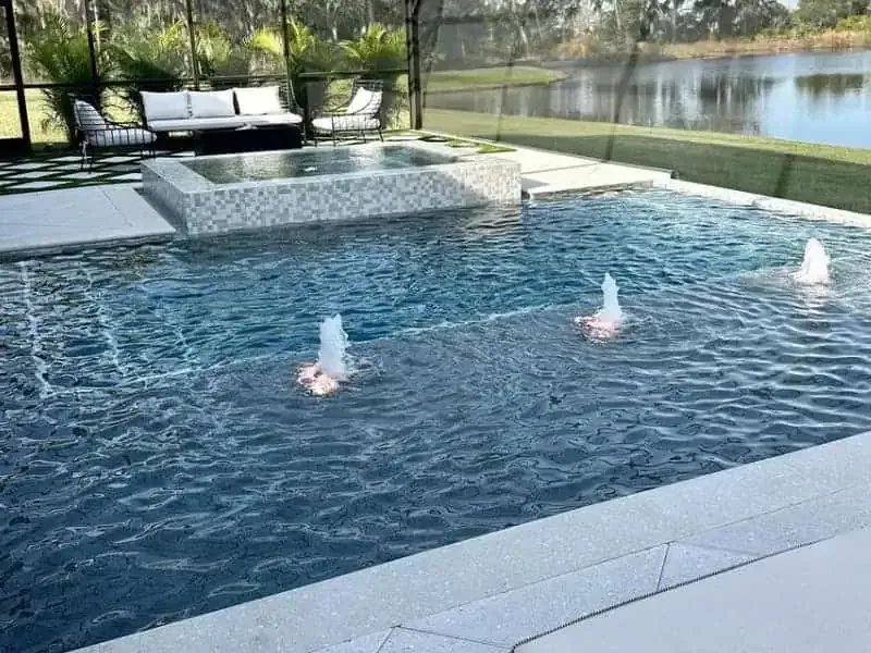 Modern outdoor pool with three water fountains and a view of the lake beyond