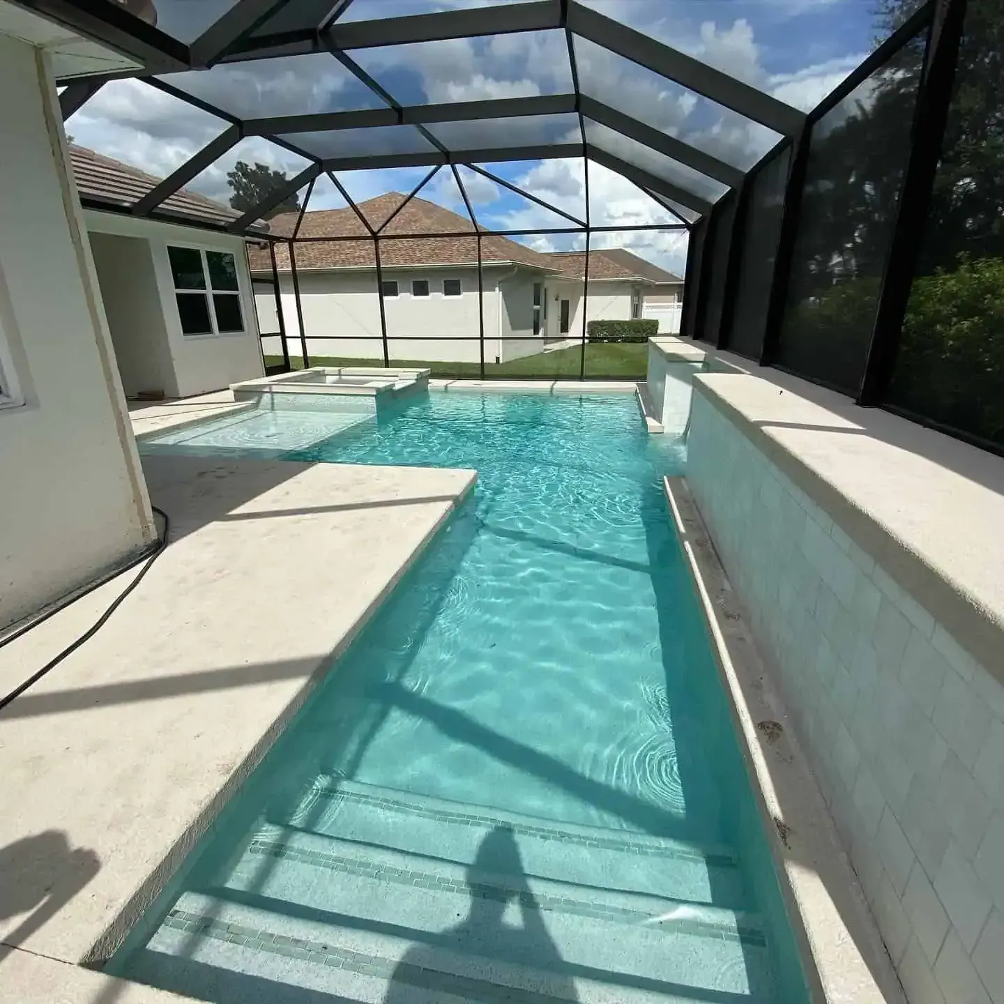 Screened-in backyard pool with turquoise water and white patio walls under a bright blue sky