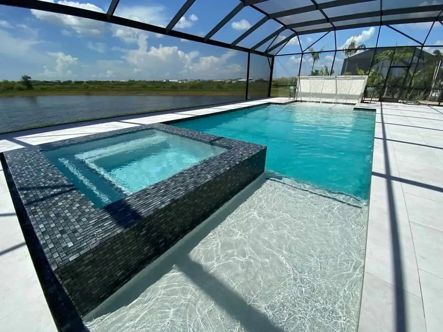 Modern outdoor pool with a raised hot tub and screened enclosure overlooking open water