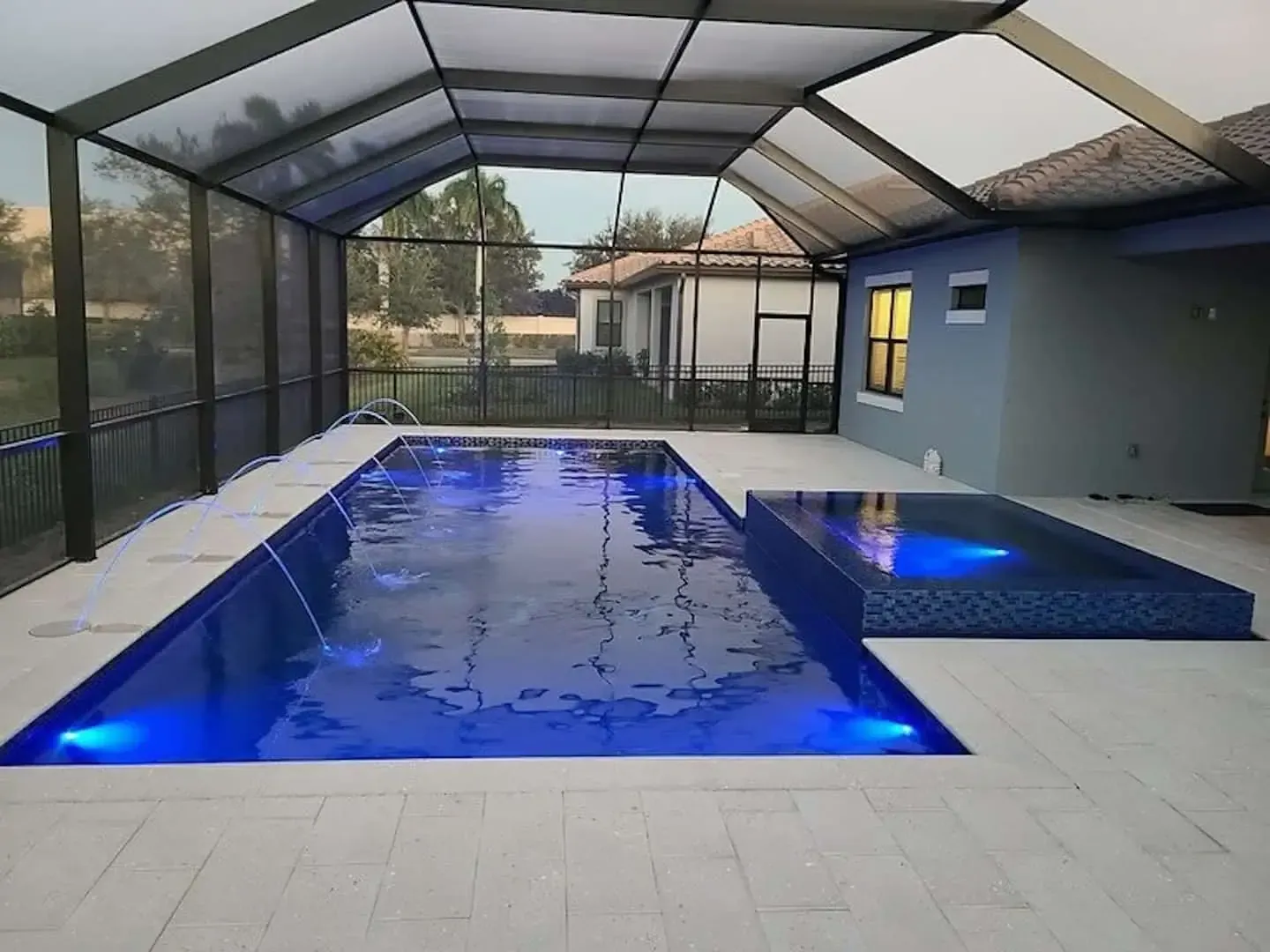 Indoor-outdoor pool with blue lighting, surrounded by a screened enclosure and tiled deck