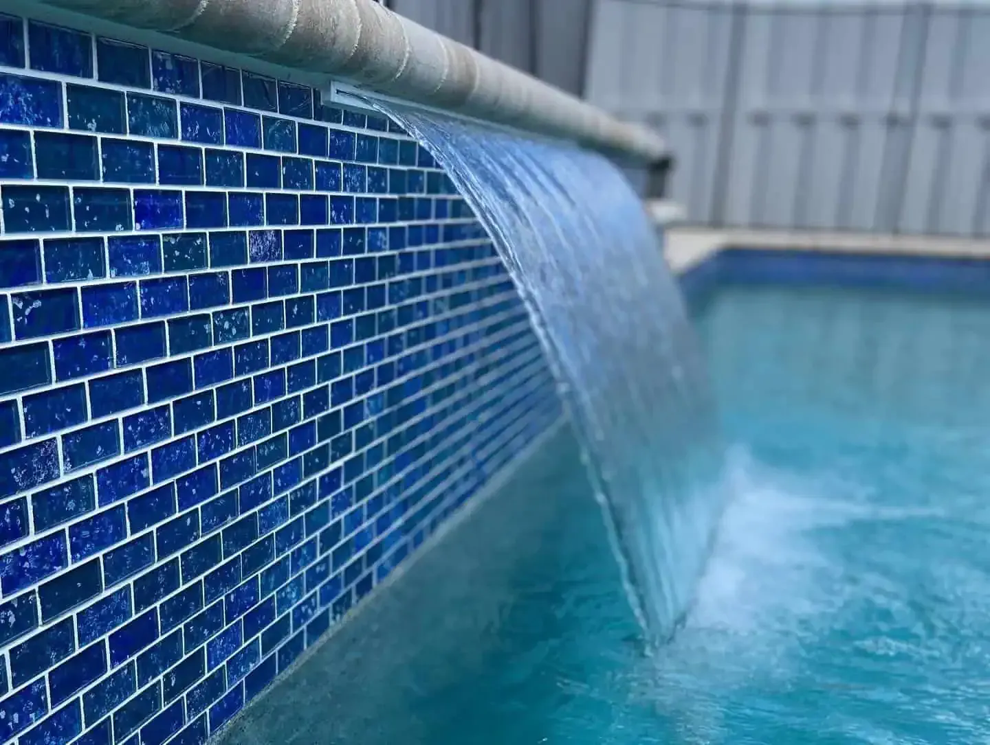 Blue-tiled pool edge with water spilling over into a swimming pool