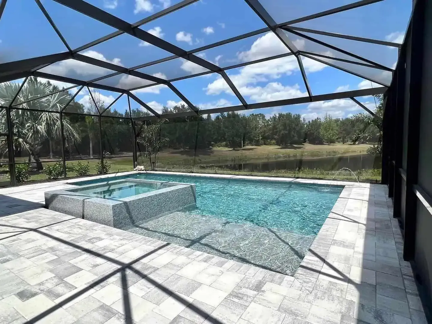 Screened-in patio with a turquoise swimming pool and hot tub under a sunny blue sky.