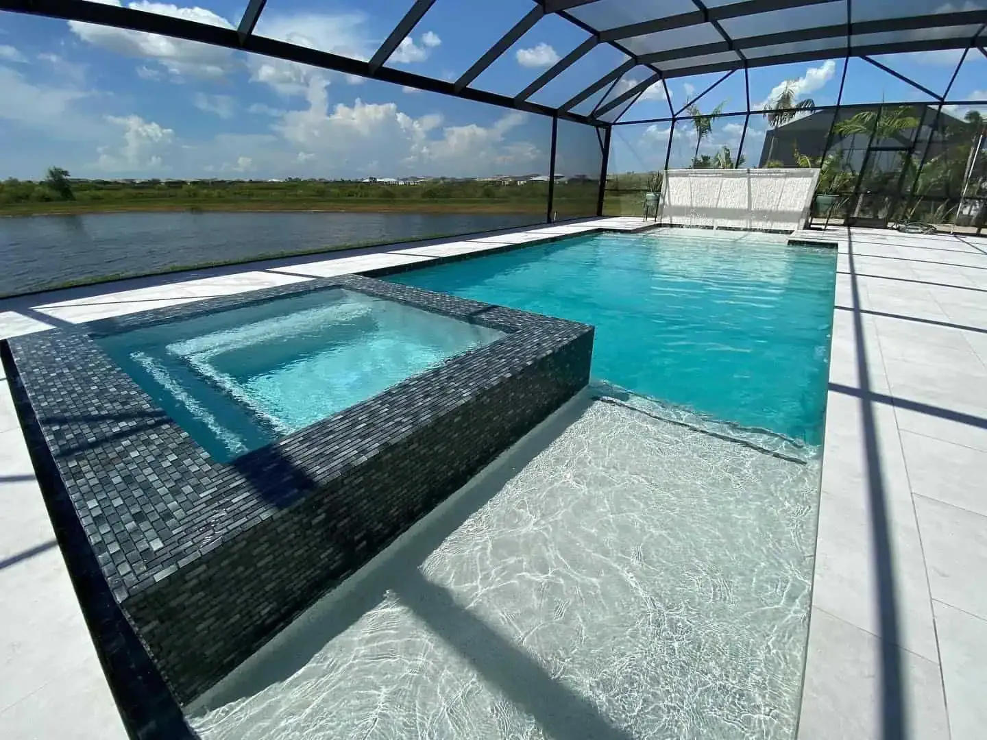 Outdoor swimming pool with a raised hot tub, turquoise water, and a screened enclosure under a sunny sky