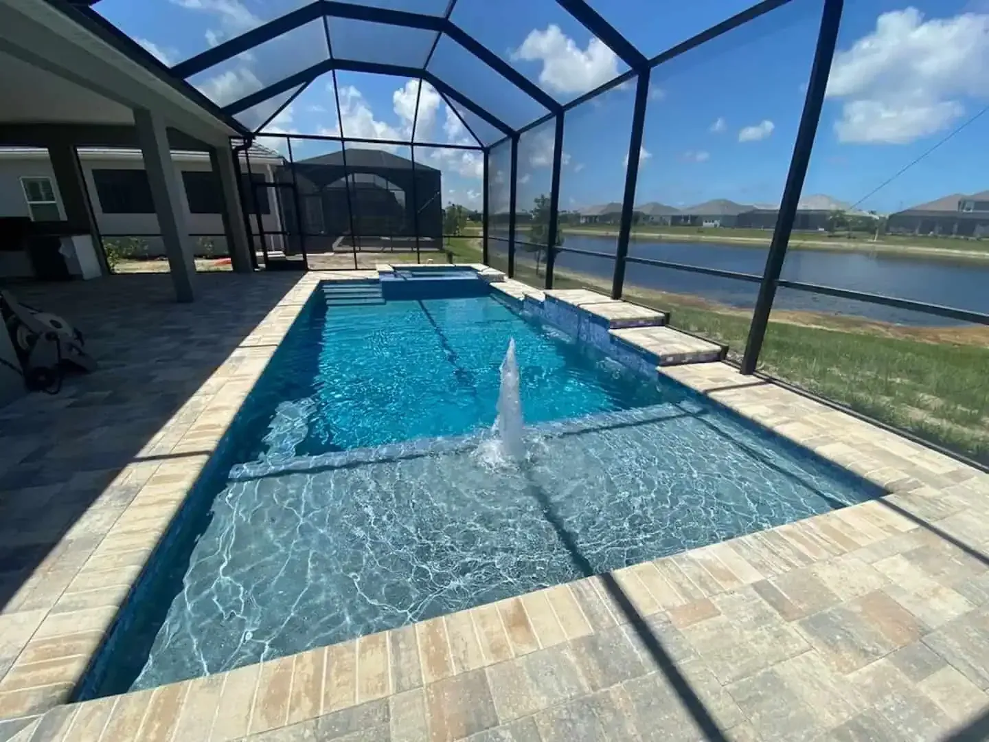 Enclosed backyard pool with fountain and water view under a screened patio on a sunny day