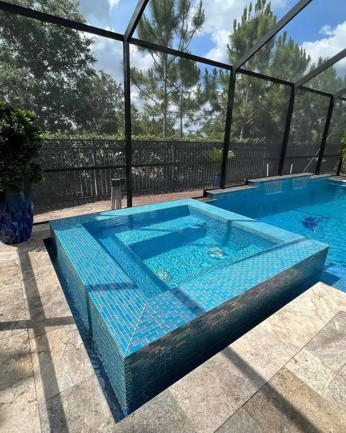 Blue mosaic hot tub beside a pool, surrounded by a screened outdoor patio and trees