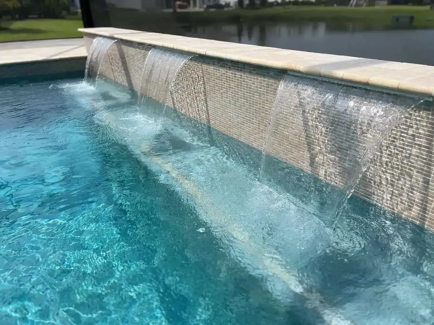 Pool waterfall spilling into blue water beside a stone wall