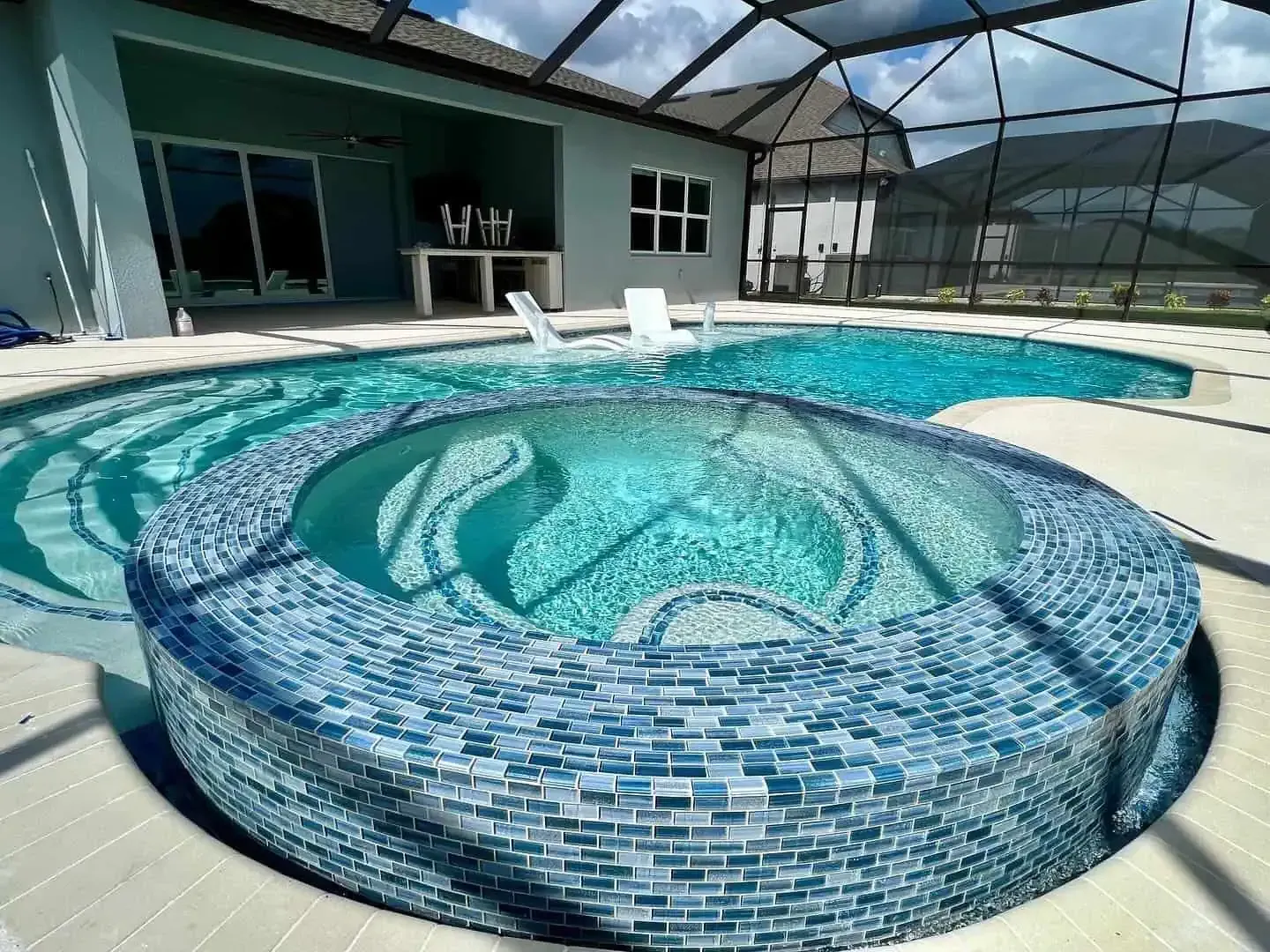 Indoor swimming pool with a raised mosaic-tiled circular spa and blue water under a screened enclosure