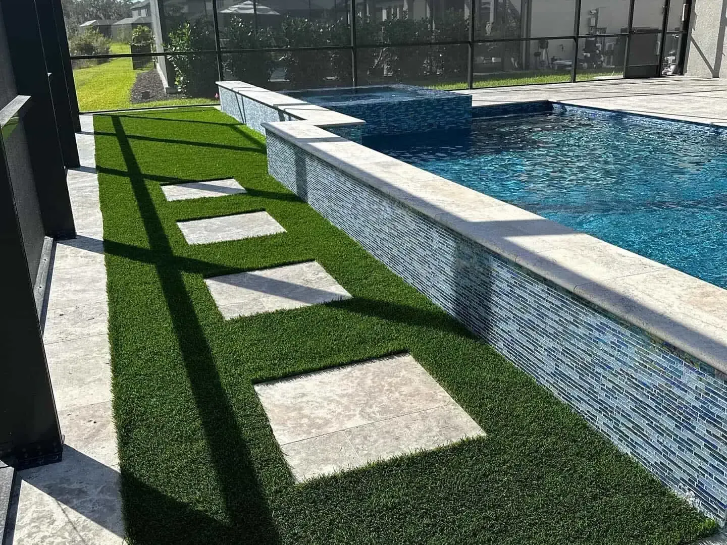 Poolside walkway with artificial turf and stepping stones beside a blue tiled pool